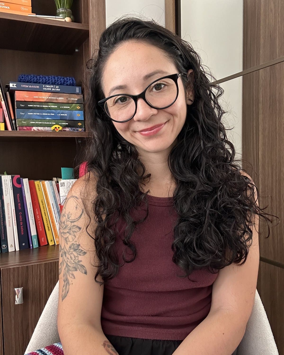 Gabriela Borda, psicóloga, sentada em uma poltrona ao lado de uma estante com livros.
